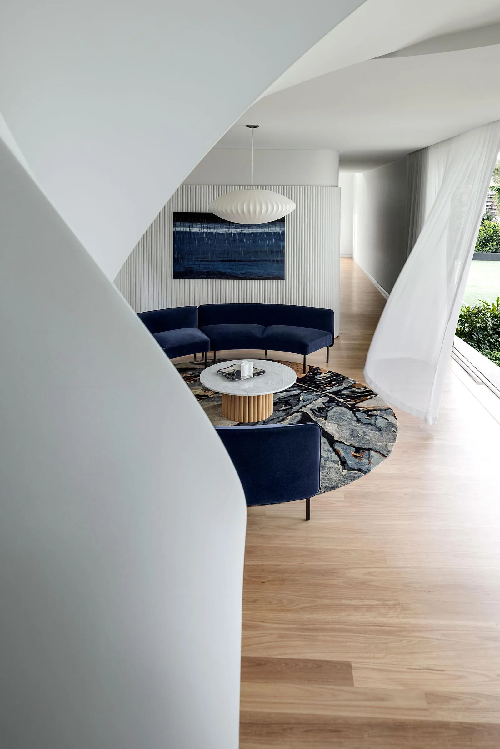 A modern living room with a dark blue fabric sectional sofa, a marble coffee table, and a round rug with a nature-inspired pa