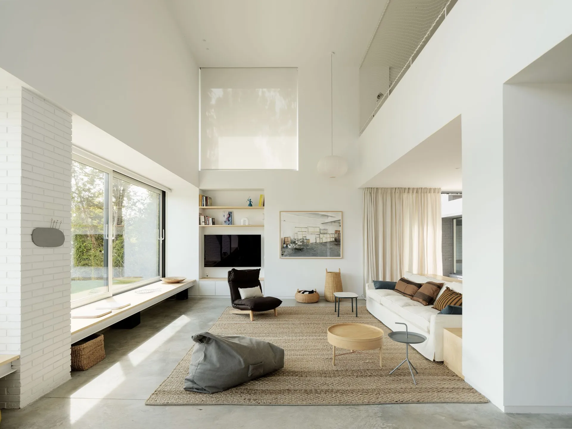 A minimalist residential living room with neutral tones, featuring a white sofa, coffee tables, and a window.