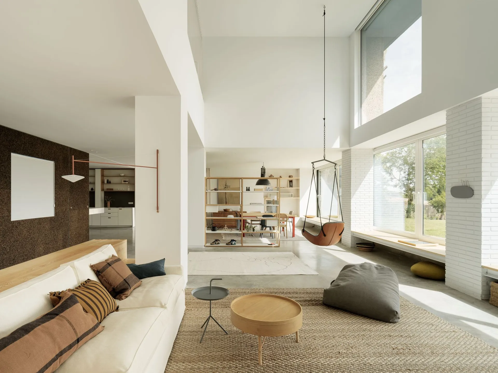 A minimalist living room with a white sofa, light wood coffee tables, and a concrete floor.