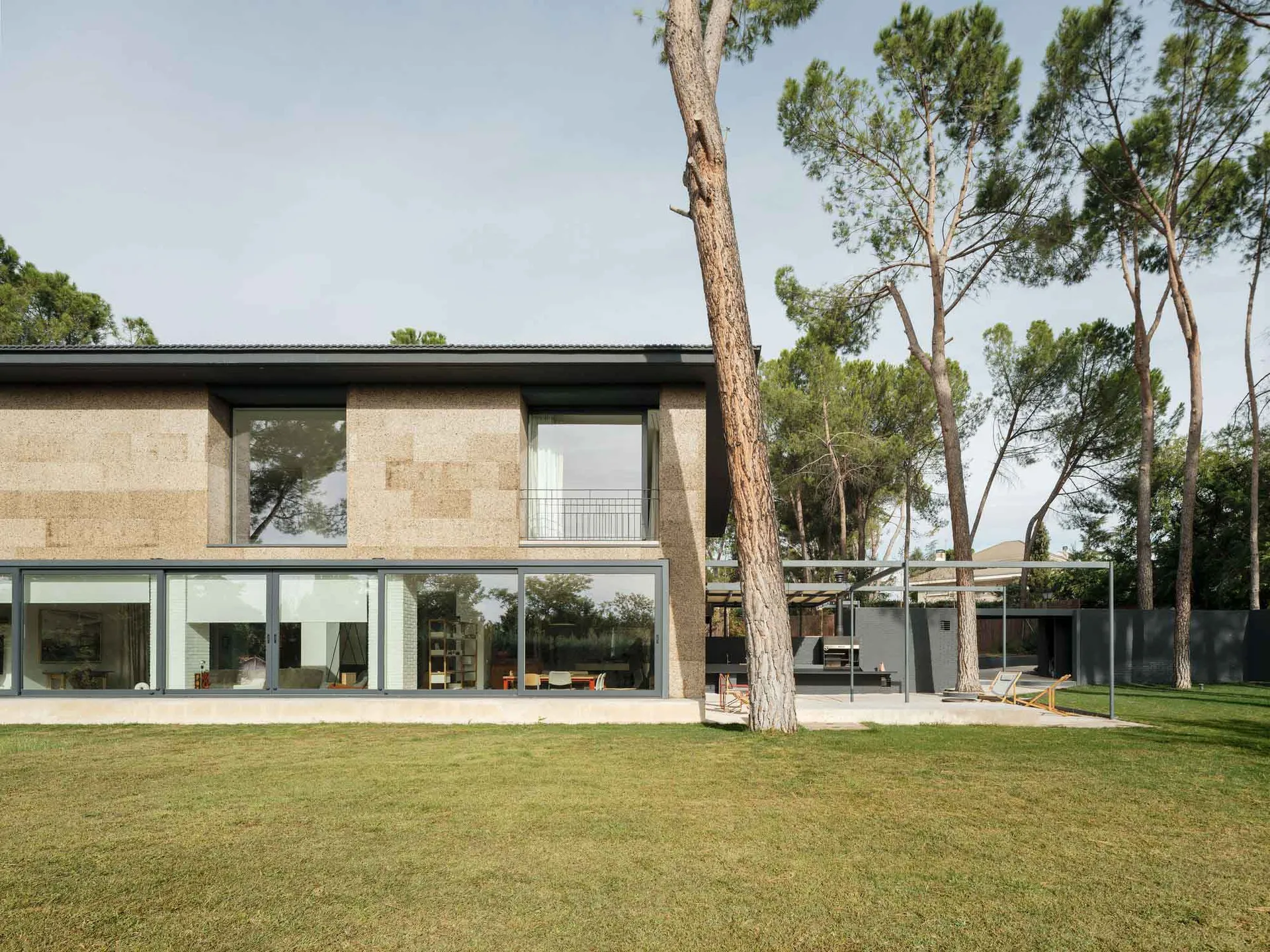 A modern house with a concrete exterior, large windows, and a lush green lawn surrounded by tall trees.