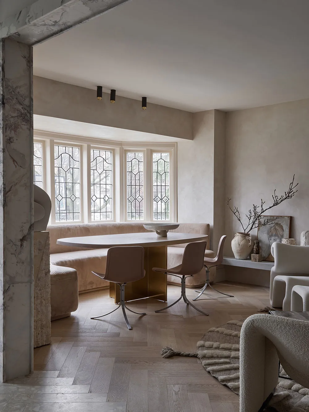 Contemporary living room featuring a wooden dining table, chairs, and sofa, with a white vase and a window with stained glass