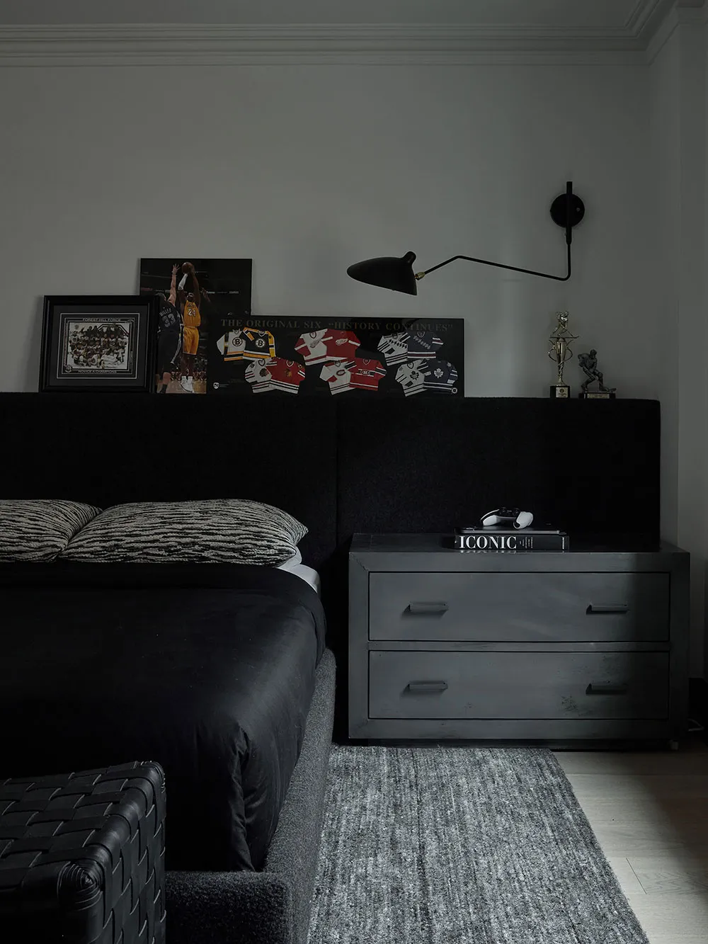 A minimalist black bedroom with a upholstered bed, black nightstand, and framed posters.