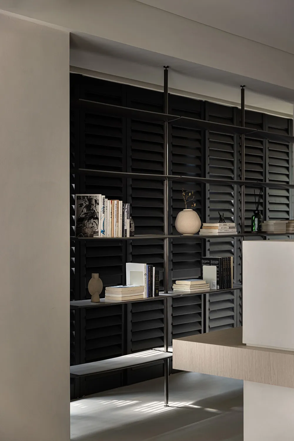 A minimalist bookshelf with black shutters and metal shelves, featuring books and decorative items.