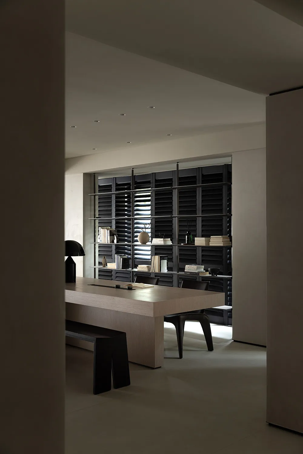 Minimalist modern workspace featuring a wooden table with a bench and black chairs, illuminated by overhead lighting, with a