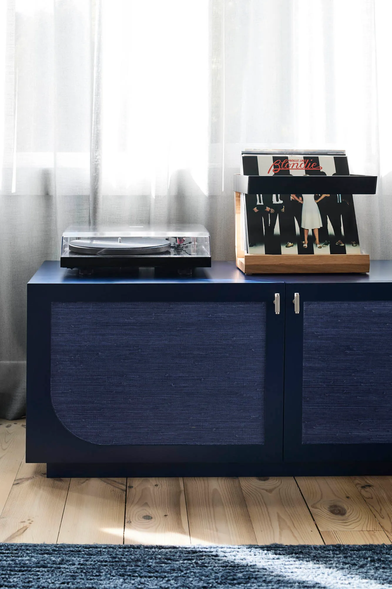 A wooden cabinet with a vinyl record player on top and a collection of vinyl records on a stand.