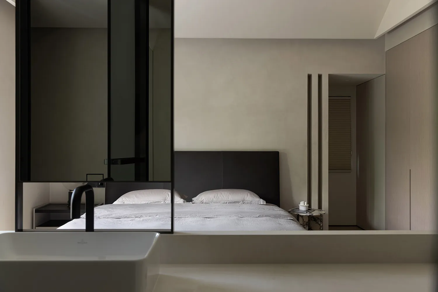 A minimalist bedroom with a white bed, black headboard, and textured walls.
