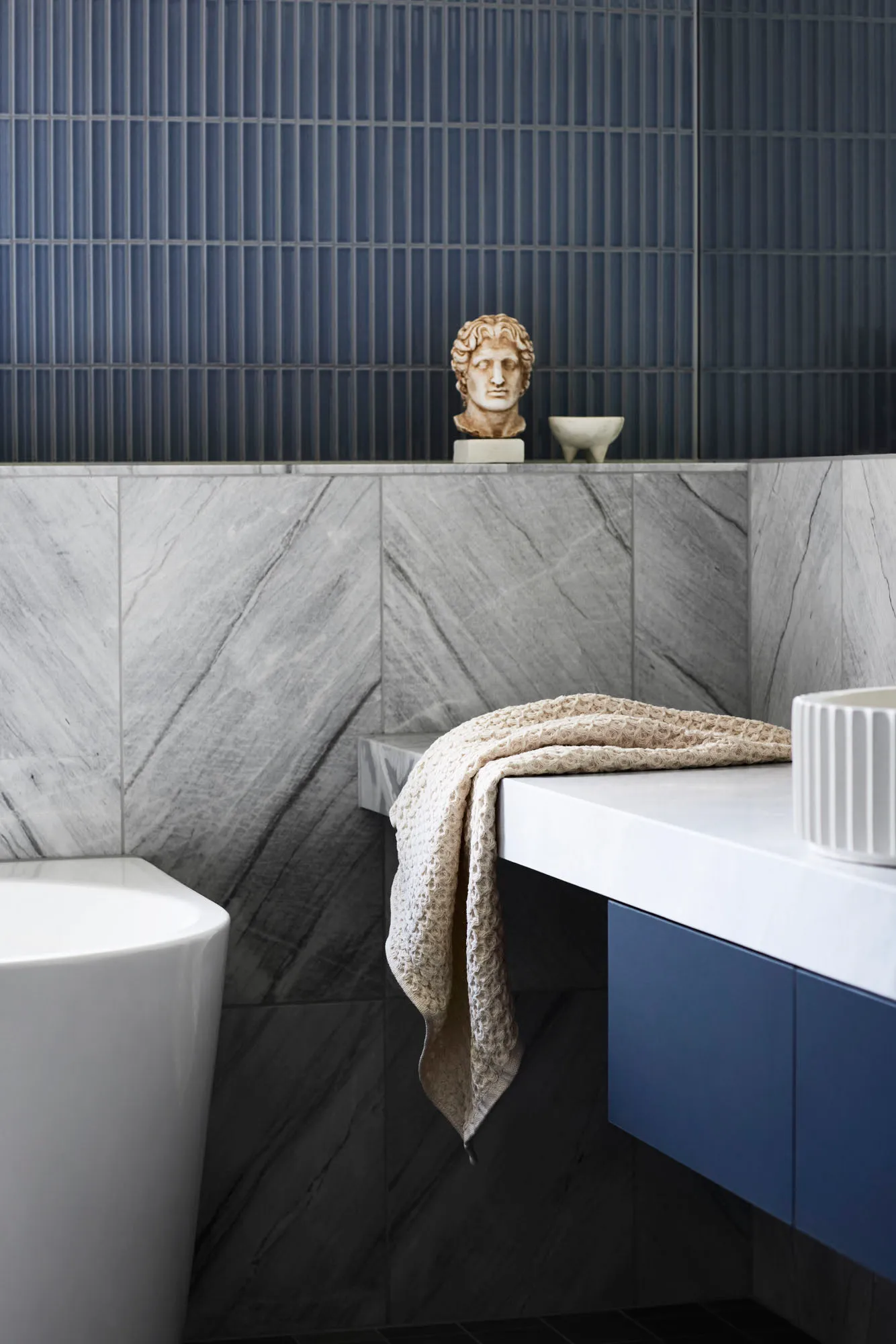 Modern bathroom featuring a freestanding bathtub, marble countertop, and a statue on the shelf.