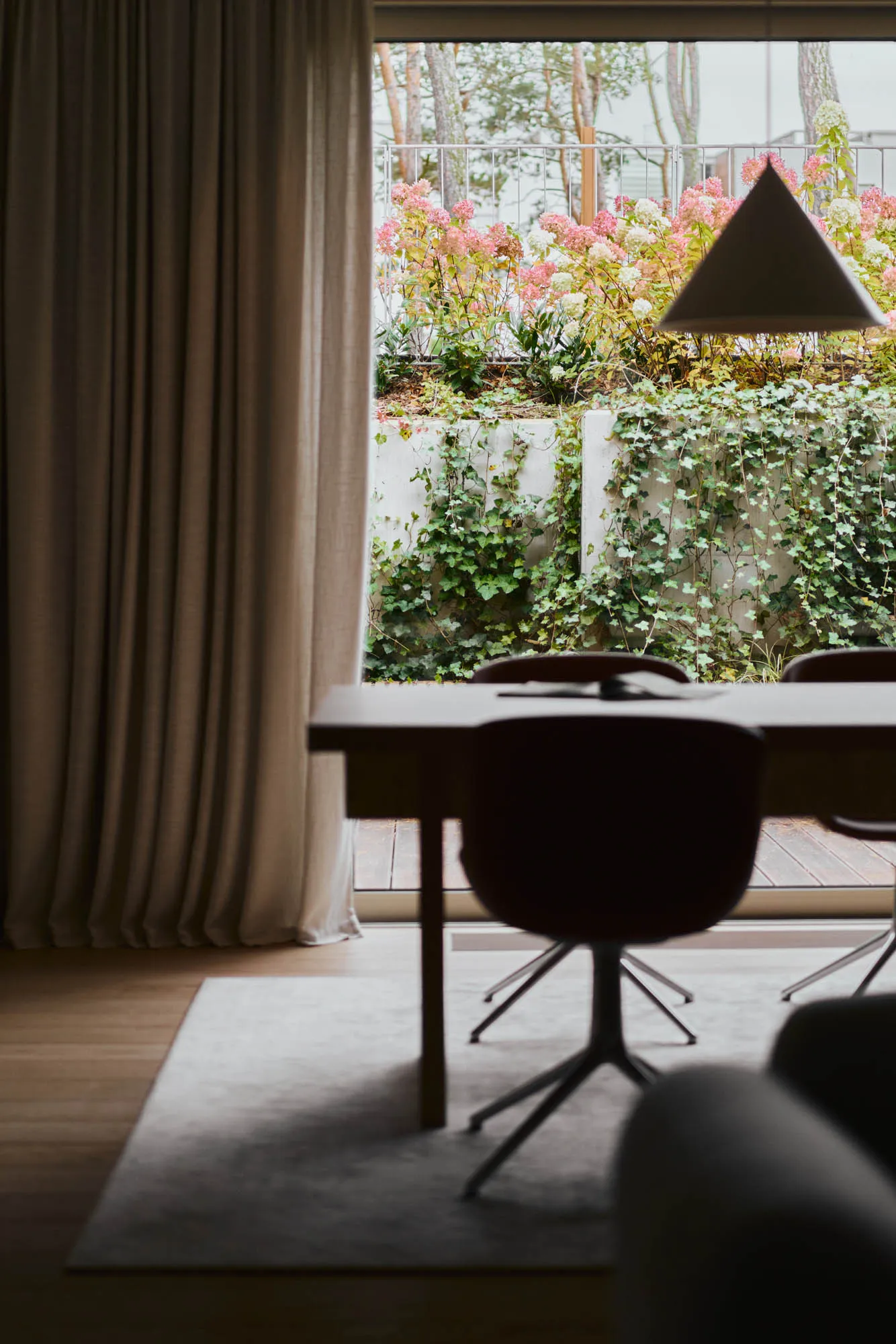 Modern dining room with wooden furniture and a floral outdoor view through a large window.