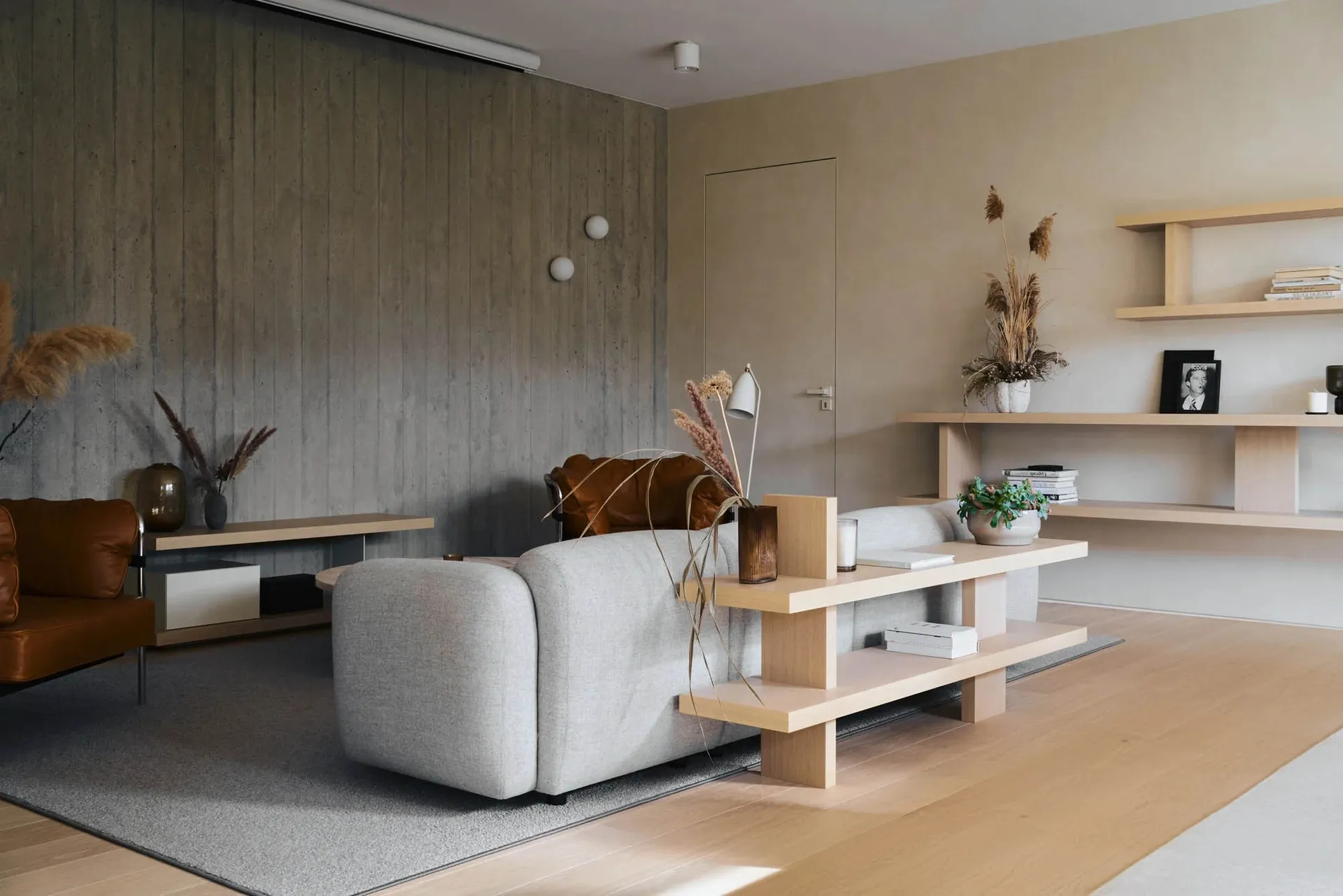 A modern minimalist living room with concrete walls, wooden shelves, and a light-colored fabric sofa.