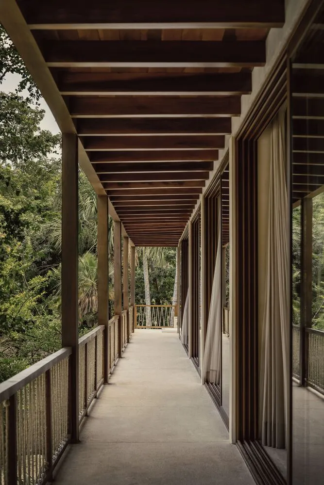 A wooden veranda patio with a roof and open sides, surrounded by tropical vegetation.