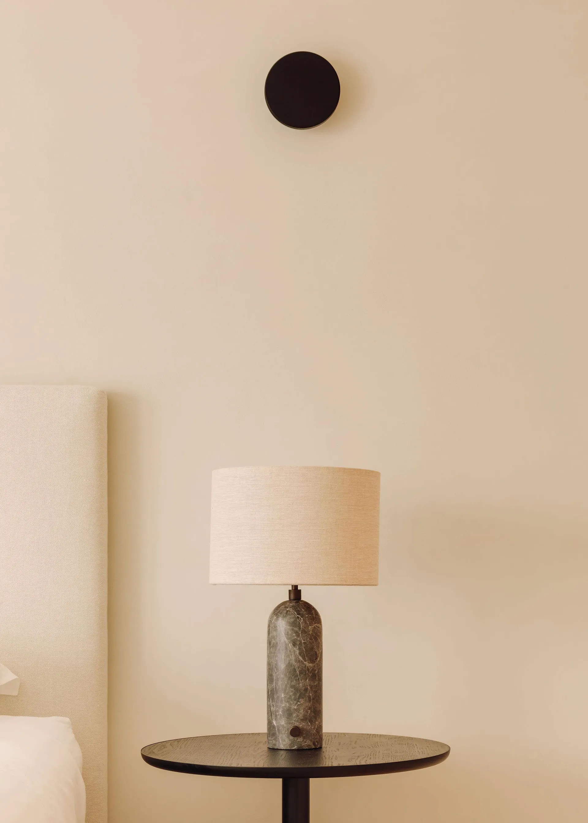 A minimalist bedside lamp with a marble base and fabric shade, placed on a small round table.