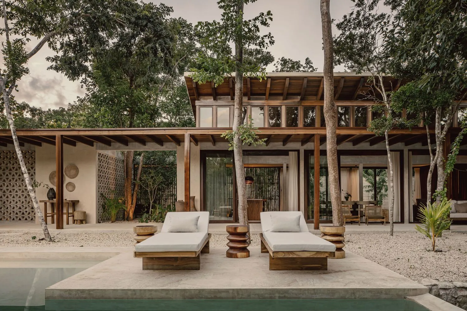 Modern residential exterior featuring a wooden house with a concrete patio, glass doors, and a swimming pool surrounded by tr