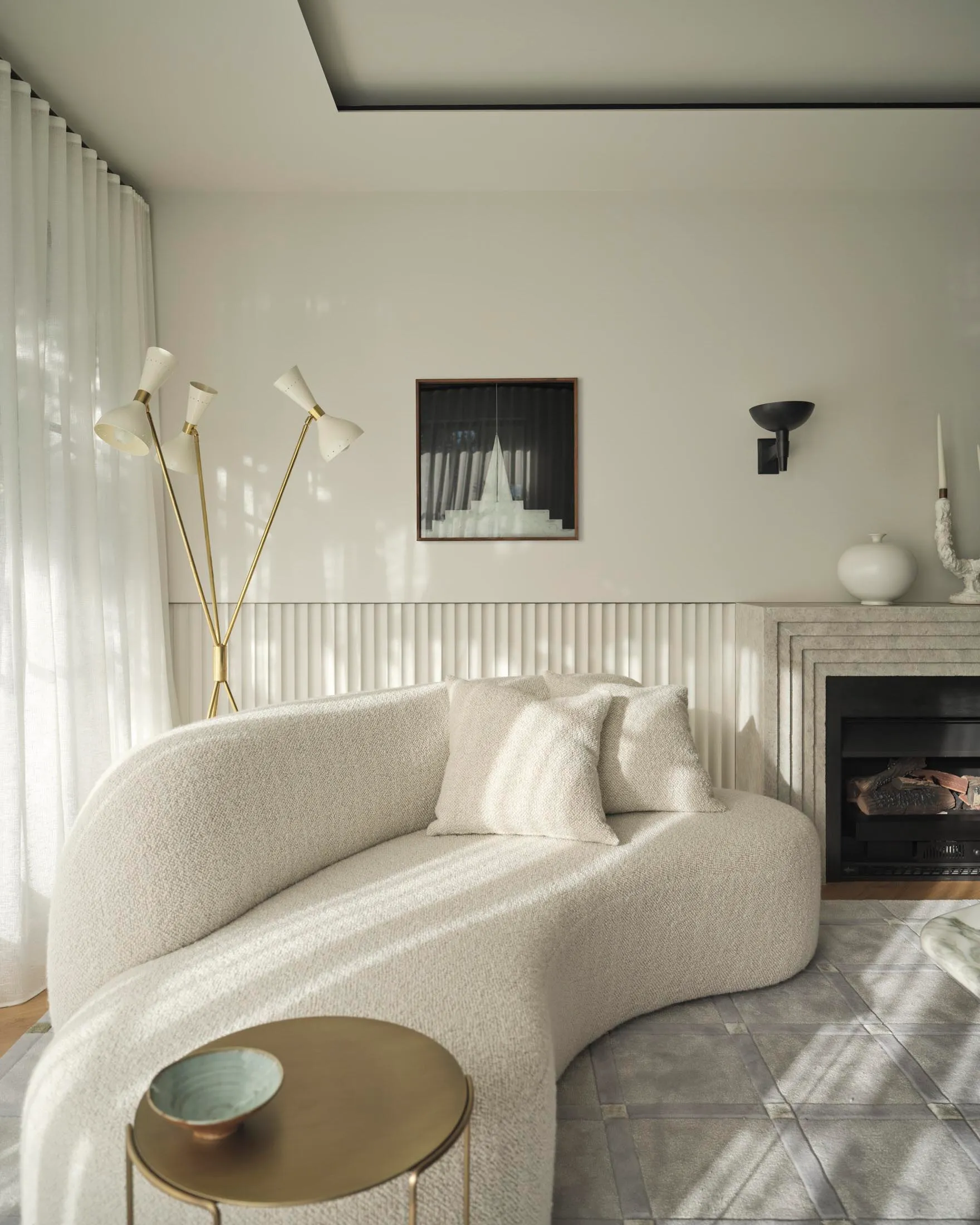 A minimalist living room with a curved sofa upholstered in textured fabric next to a fireplace with white curtains and modern
