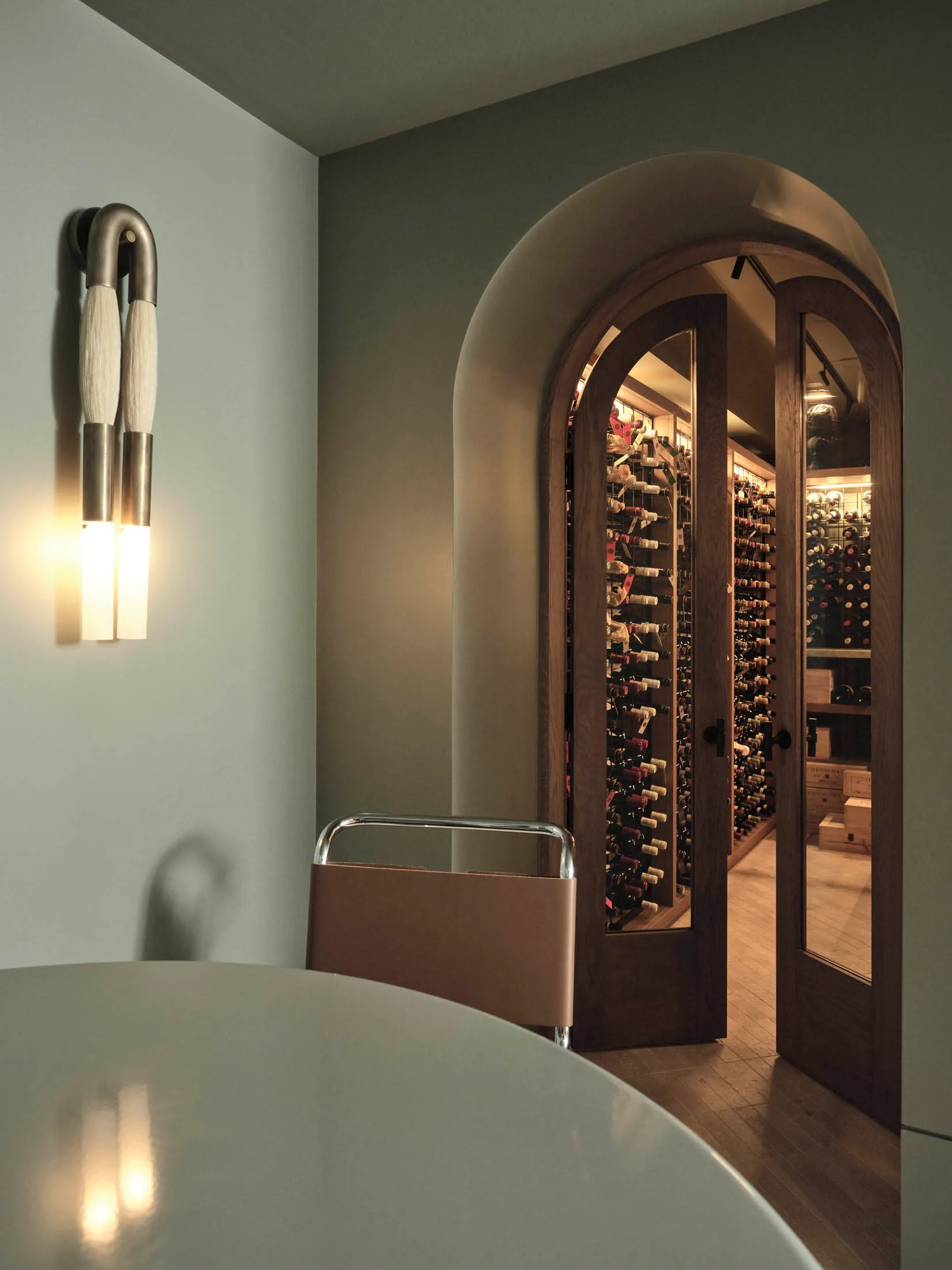 A minimalist wine cellar entrance featuring arched wooden doors and a curved wooden table.