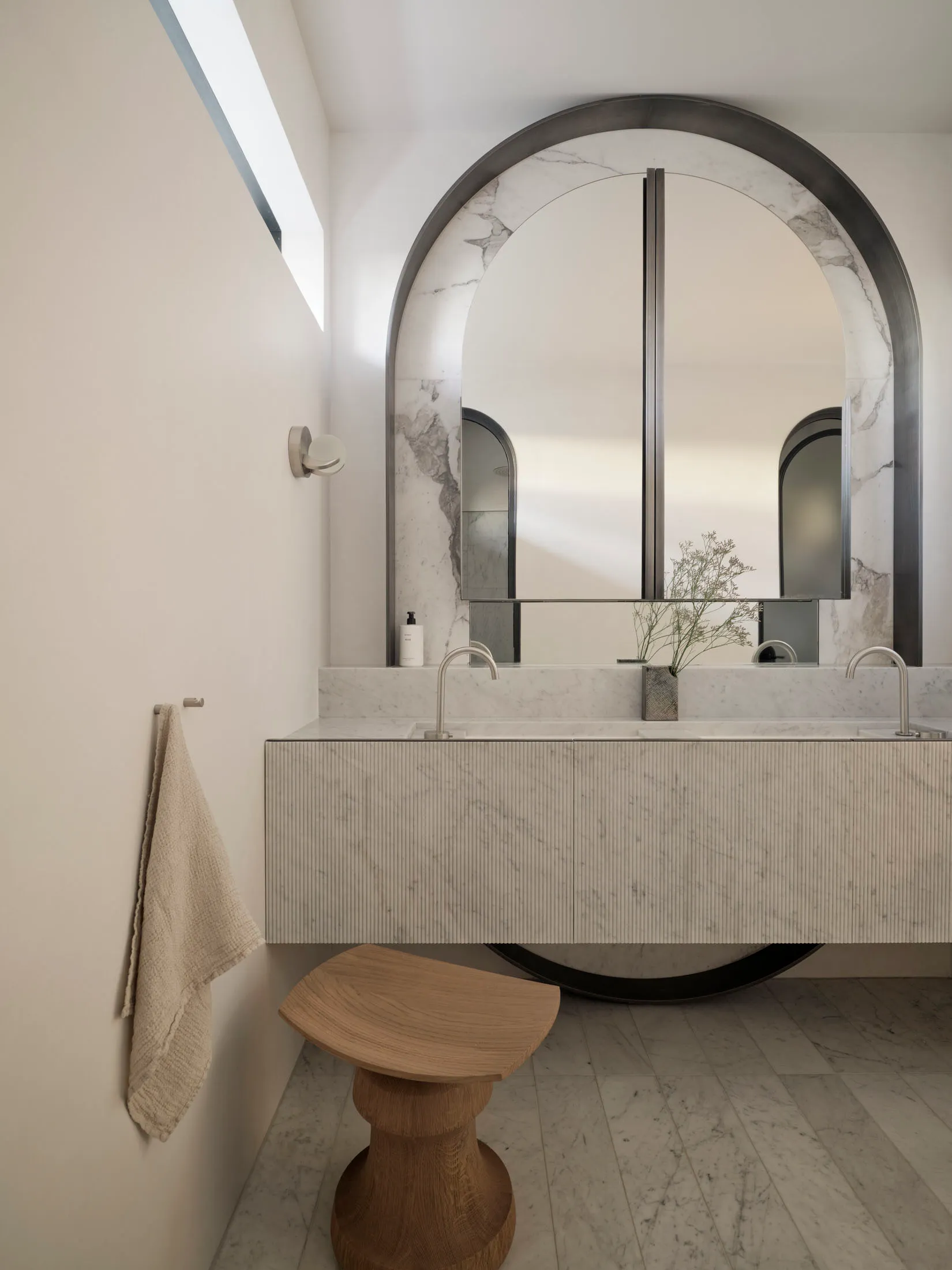Modern bathroom with marble walls, a floating vanity, and an arched mirror.