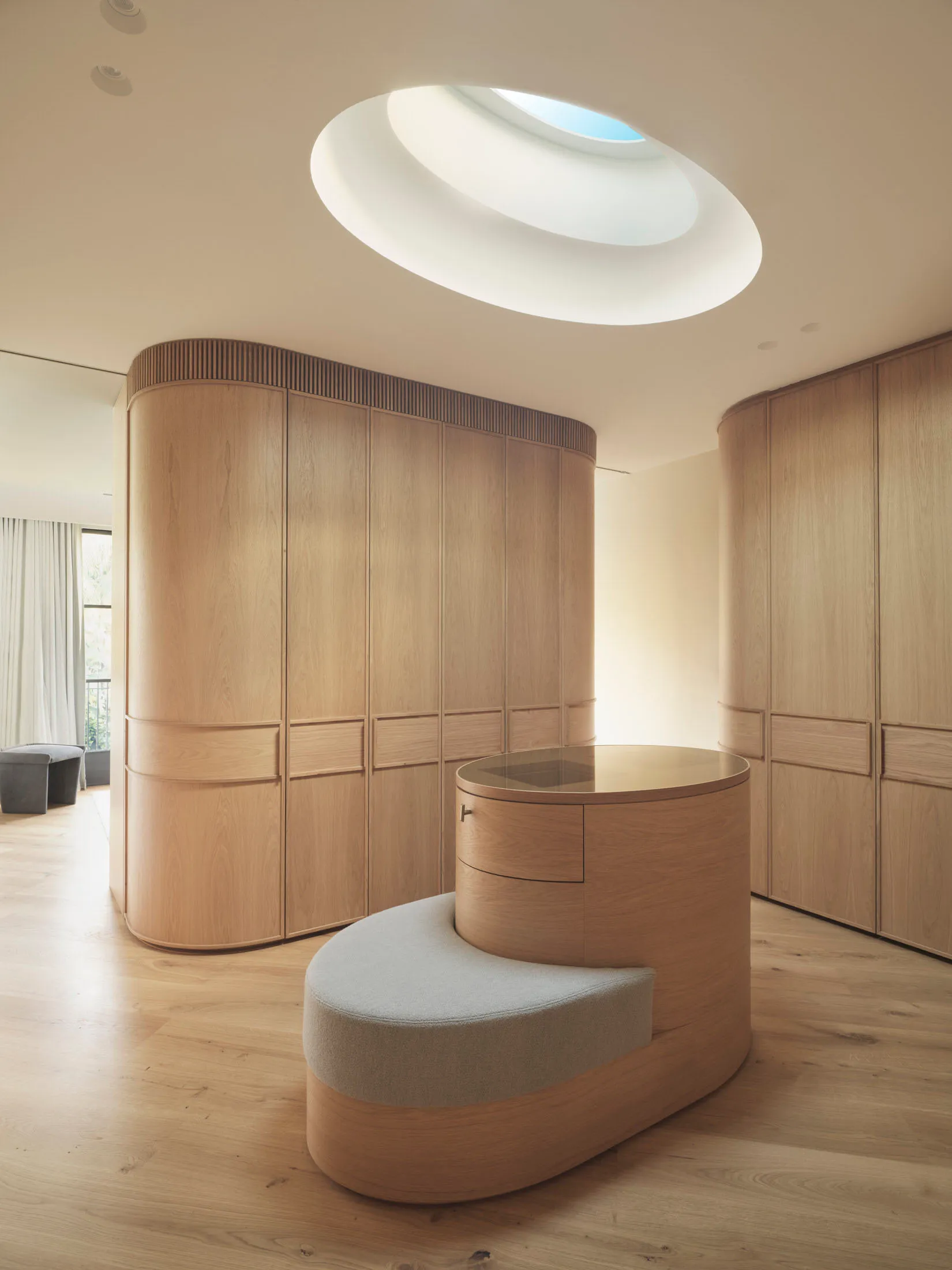 Minimalist wooden wardrobe room featuring a round glass-topped table and a curved skylight on the ceiling.