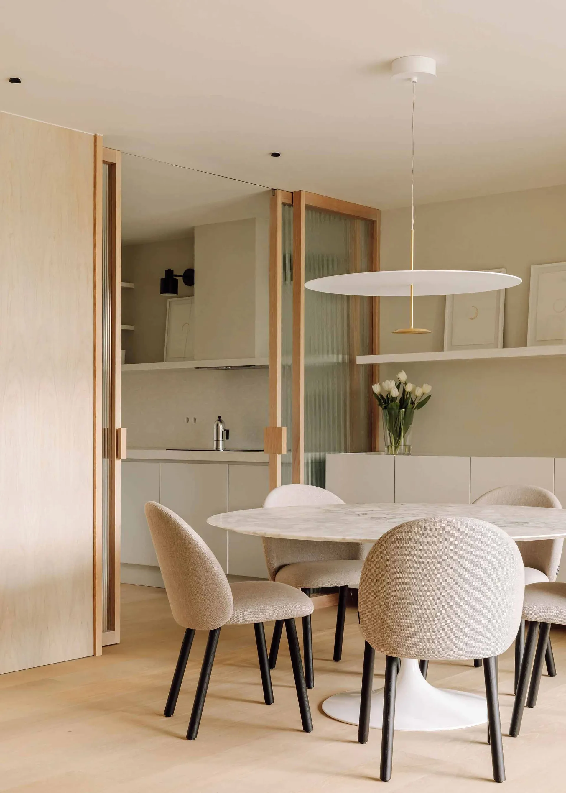 Modern minimalist kitchen with a glass table and upholstered chairs.