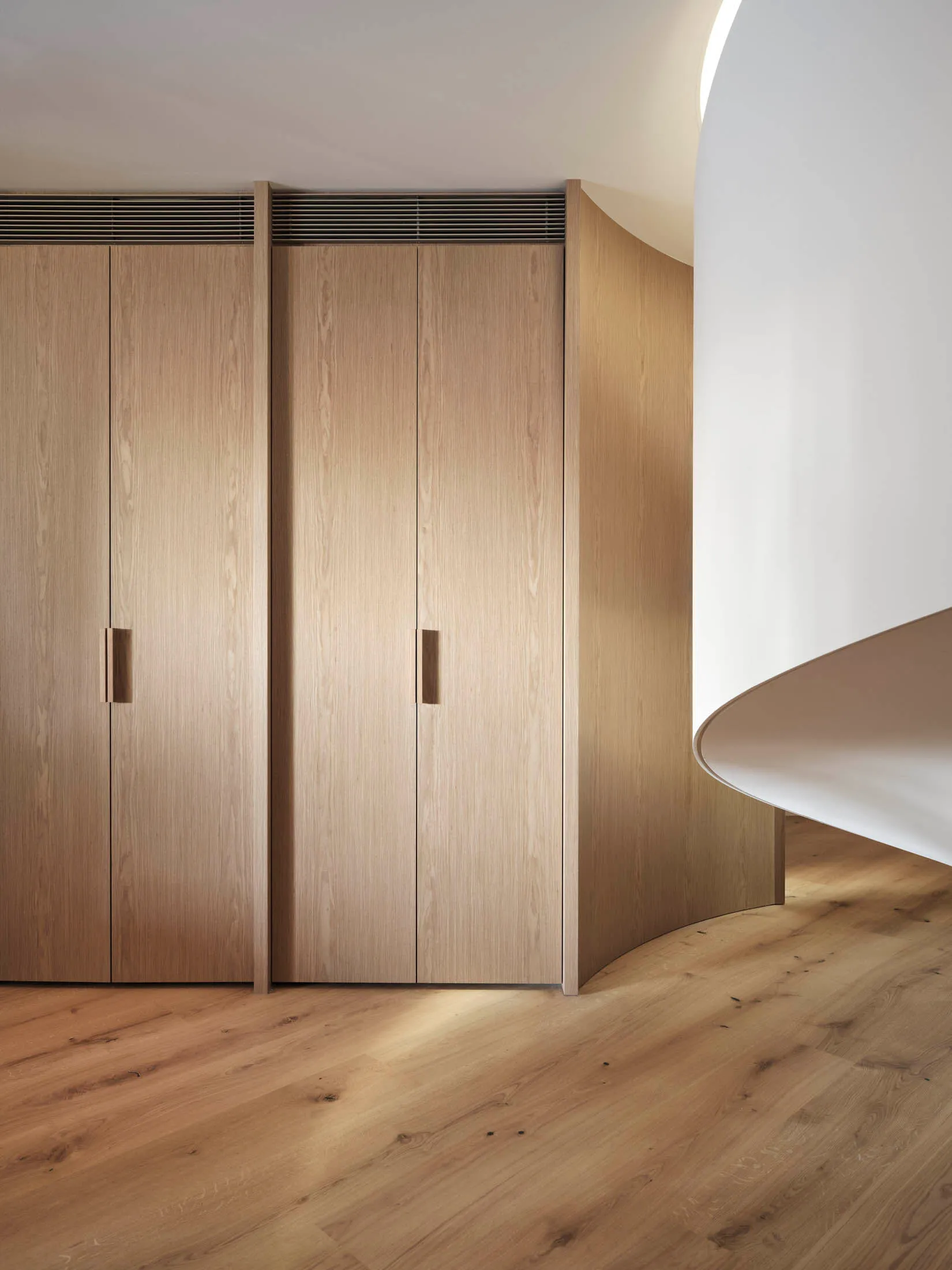 A minimalist closet with wooden cabinets and a curved wall in a residential setting.