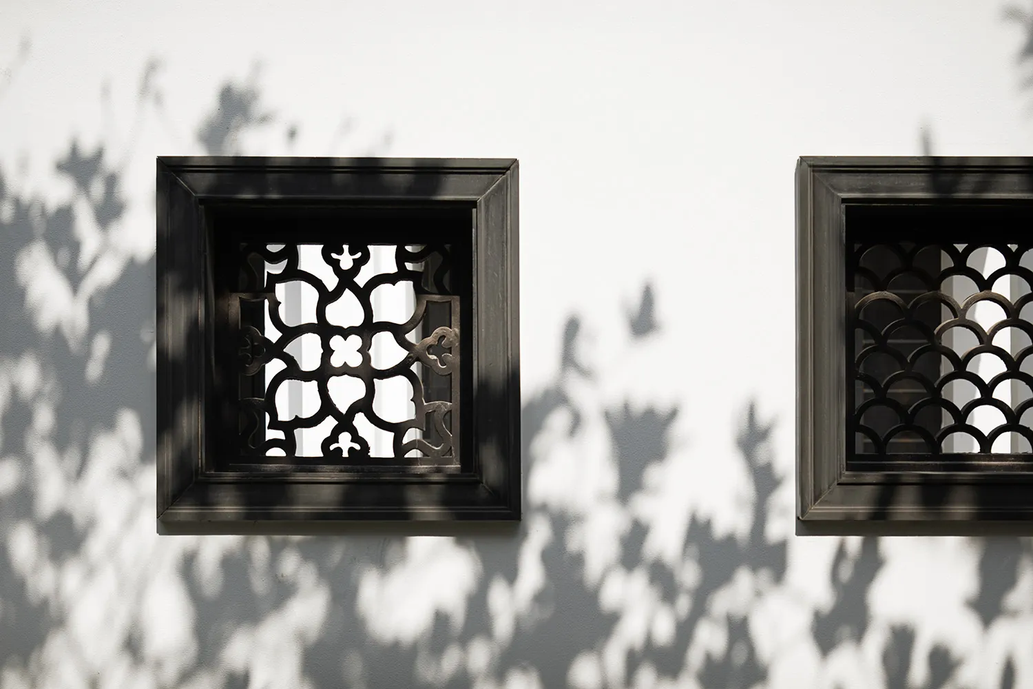White wall with geometric patterned windows and metal frames casting shadows.