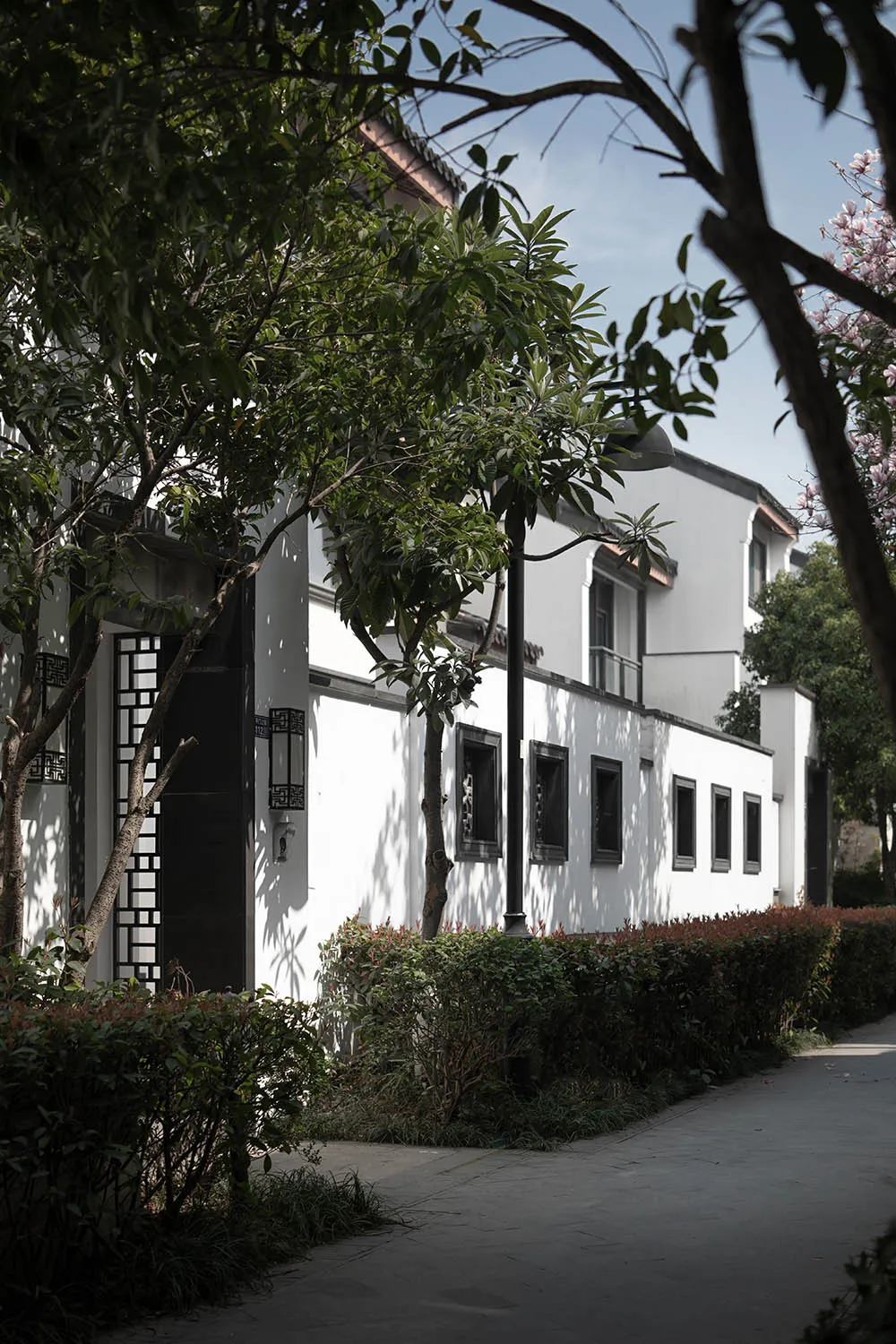 White-painted timber-frame house surrounded by green foliage and a paved pathway.