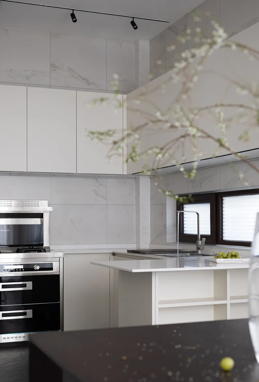 A modern minimalist residential kitchen with white cabinetry, marble countertops, and stainless steel appliances.
