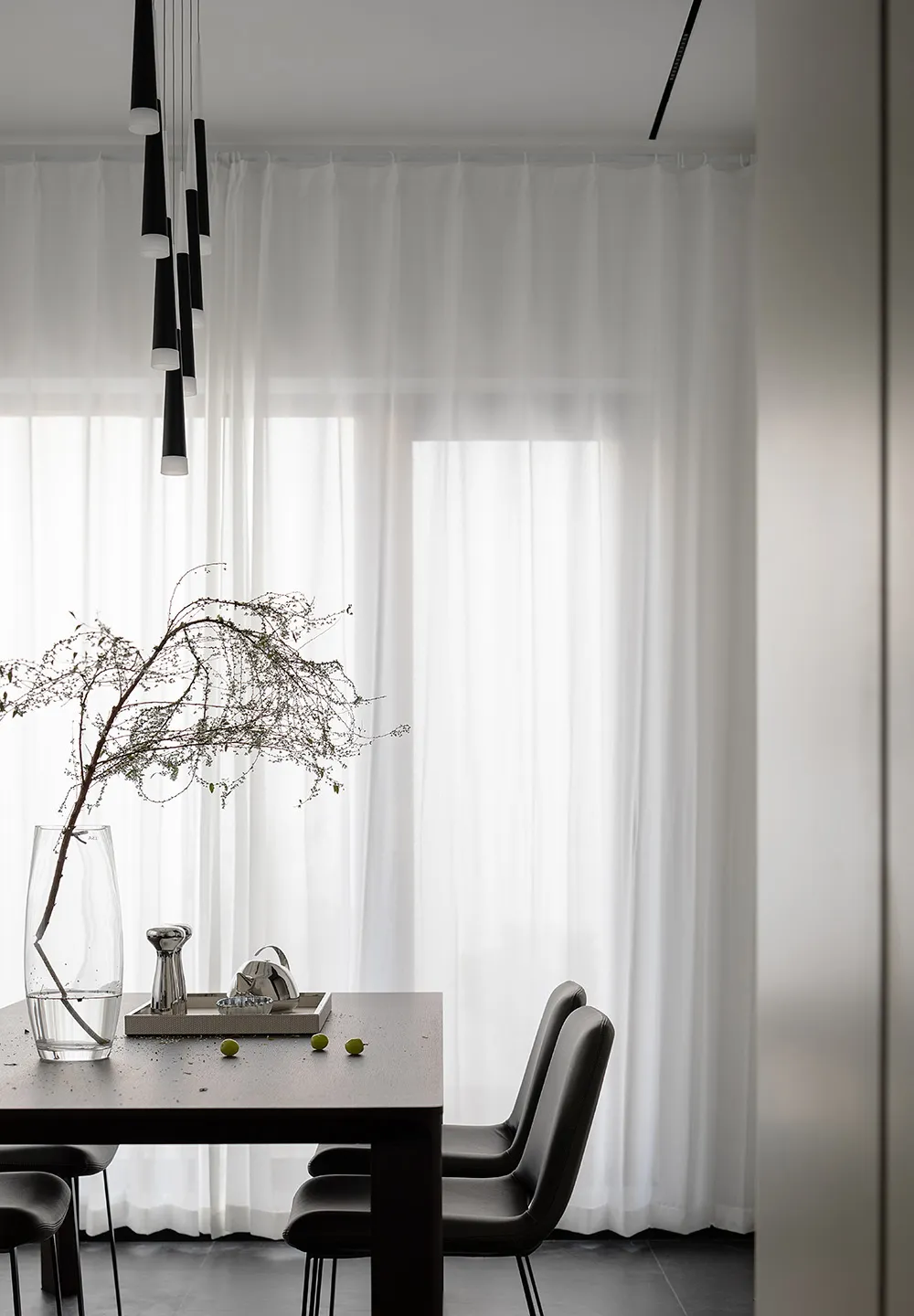 Modern minimalist dining room featuring a dark wooden table, black leather chairs, and minimalistic decor.