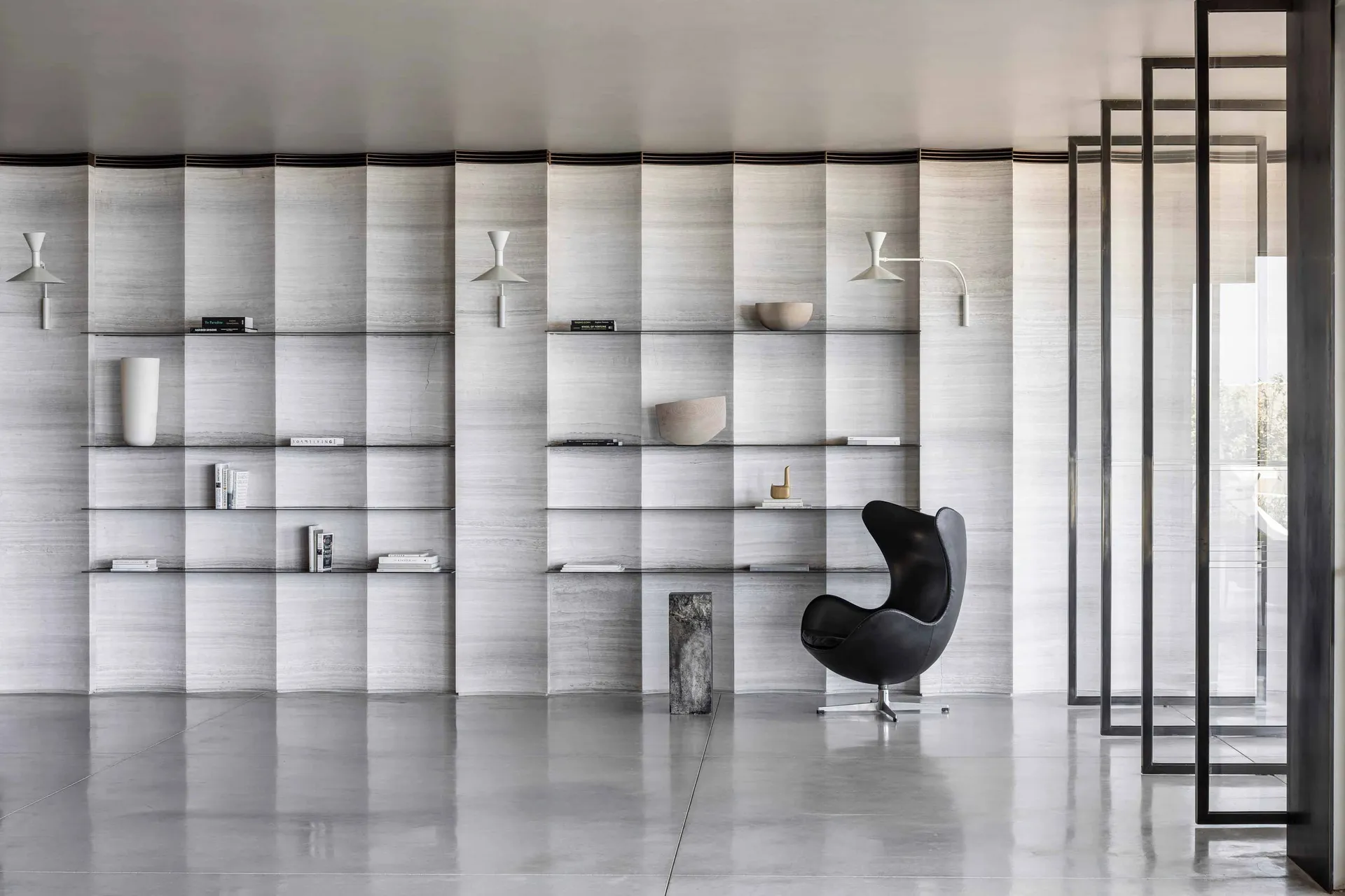 A minimalist bedroom featuring concrete walls, glass shelving, and a black armchair.