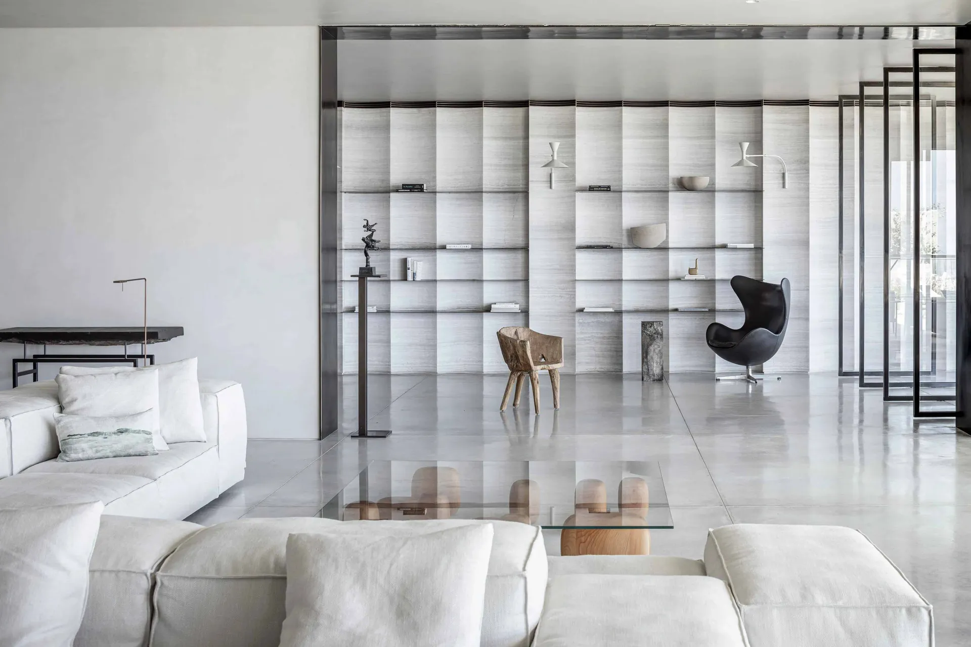 A modern living room with concrete walls, white furniture, and a glass coffee table.