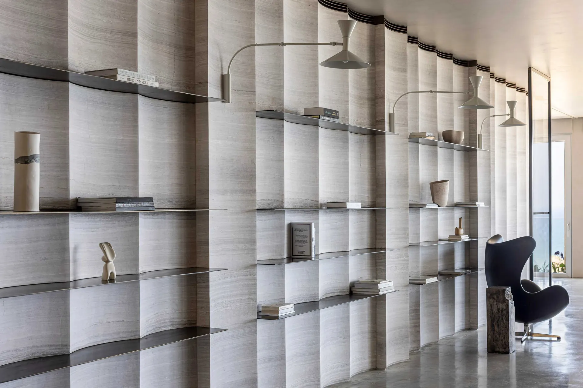 A minimalist library interior featuring curved, marble shelves and concrete columns.