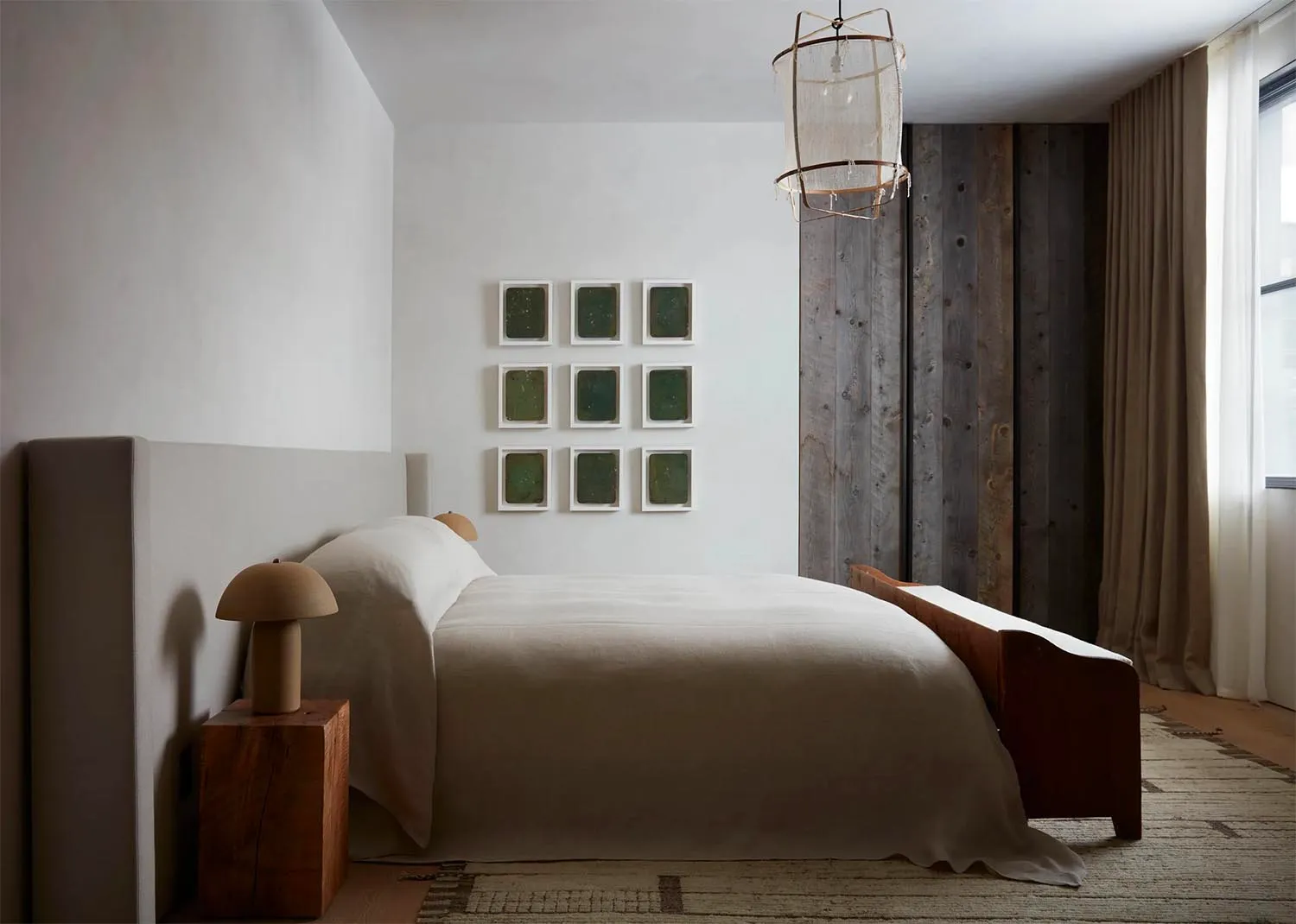 A minimalist bedroom with a white bed covered in textured cotton bedding, framed artwork on the wall, and a wooden headboard.