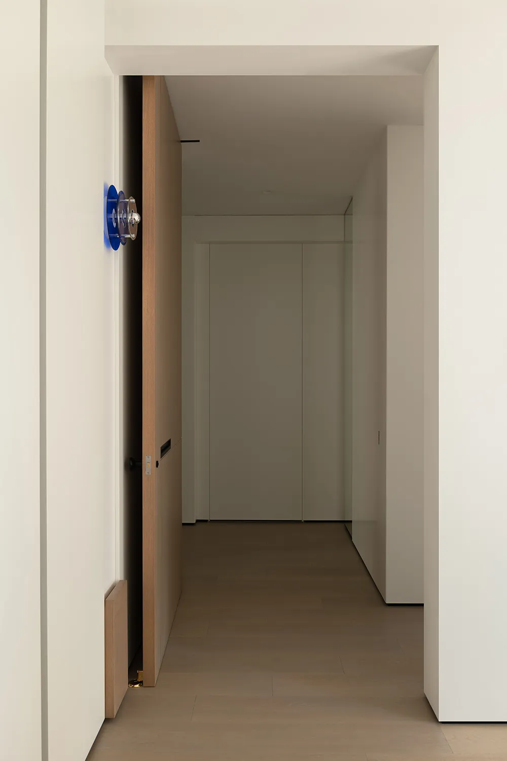 A minimalist corridor with wooden flooring and white walls.