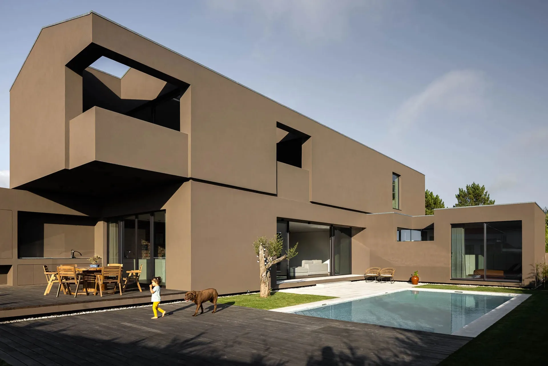 Modern residential home featuring concrete architecture with a swimming pool and a child walking with a dog.