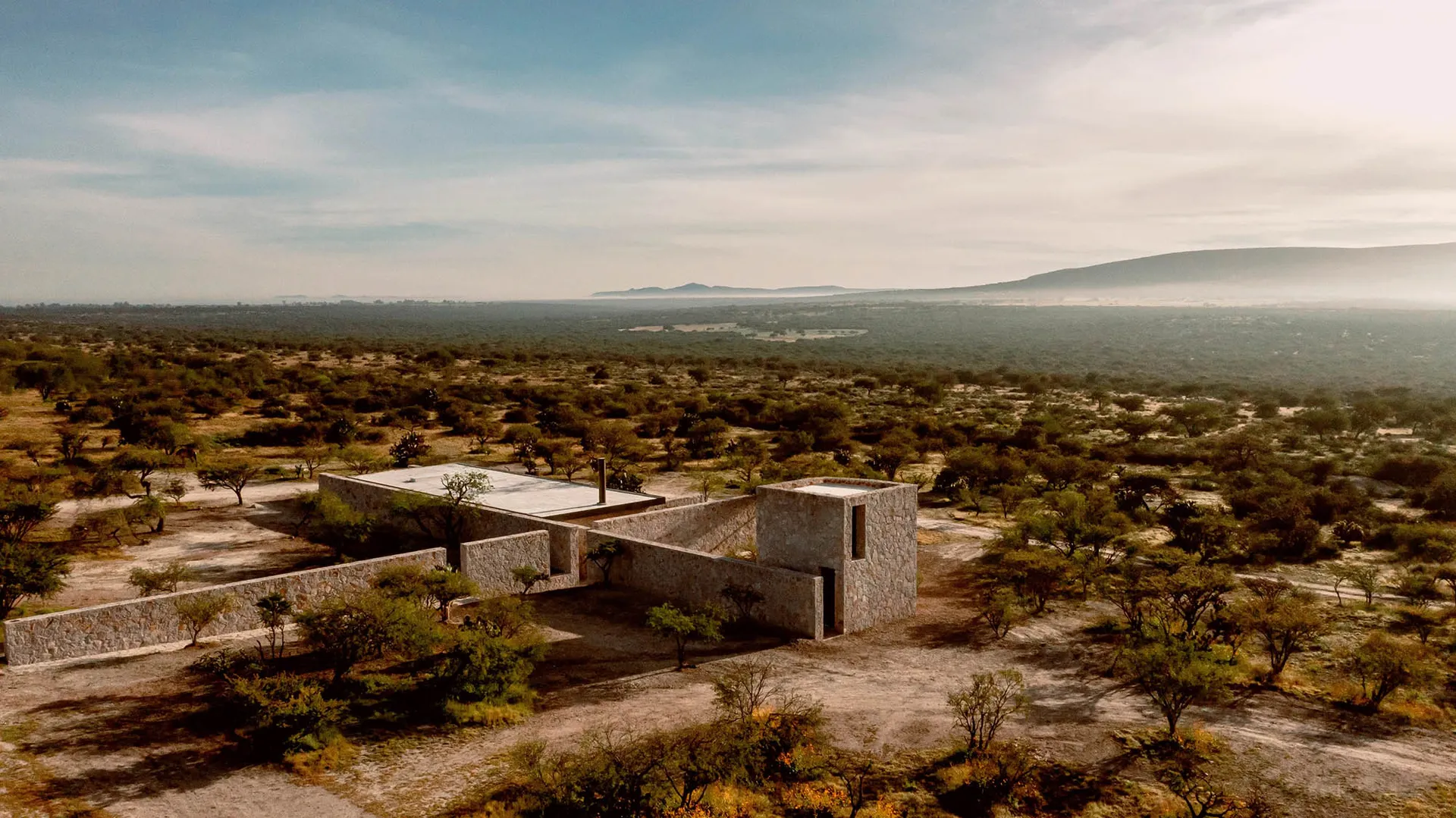 A modern stone house surrounded by trees in a desert landscape.