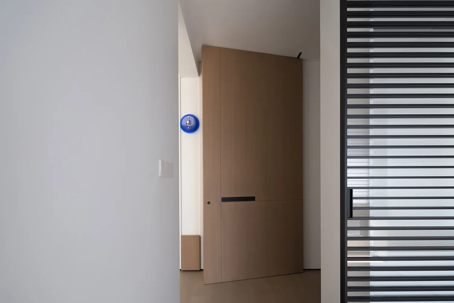 A modern wooden doorway with a blue circular detail on a white wall.