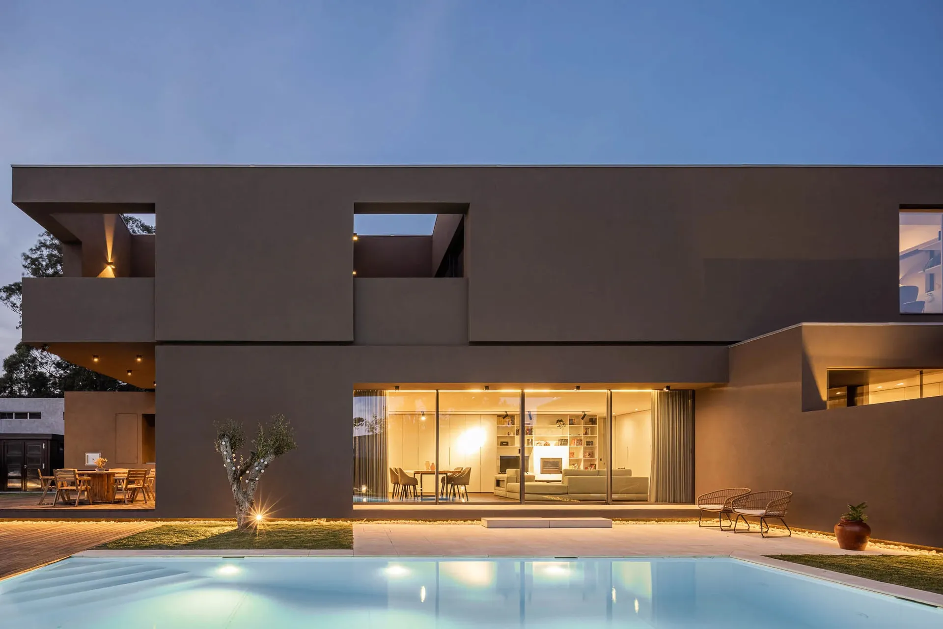An exterior view of a modern house featuring concrete walls and a courtyard with a swimming pool, illuminated at night with w