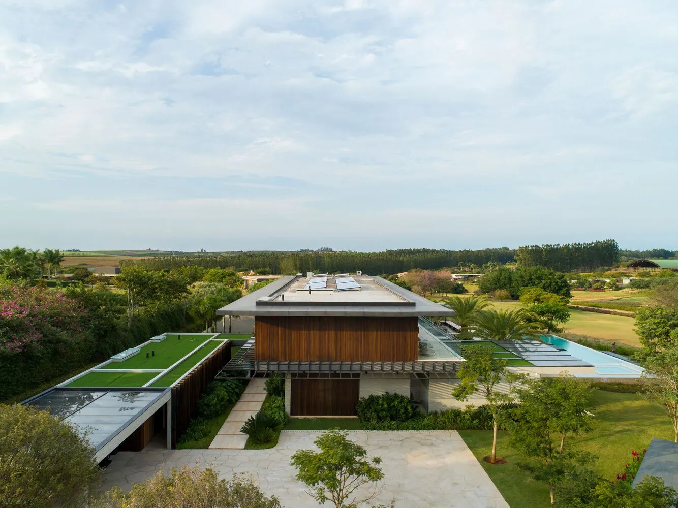 Modern residential exterior featuring large glass windows, wooden accents, and lush greenery.