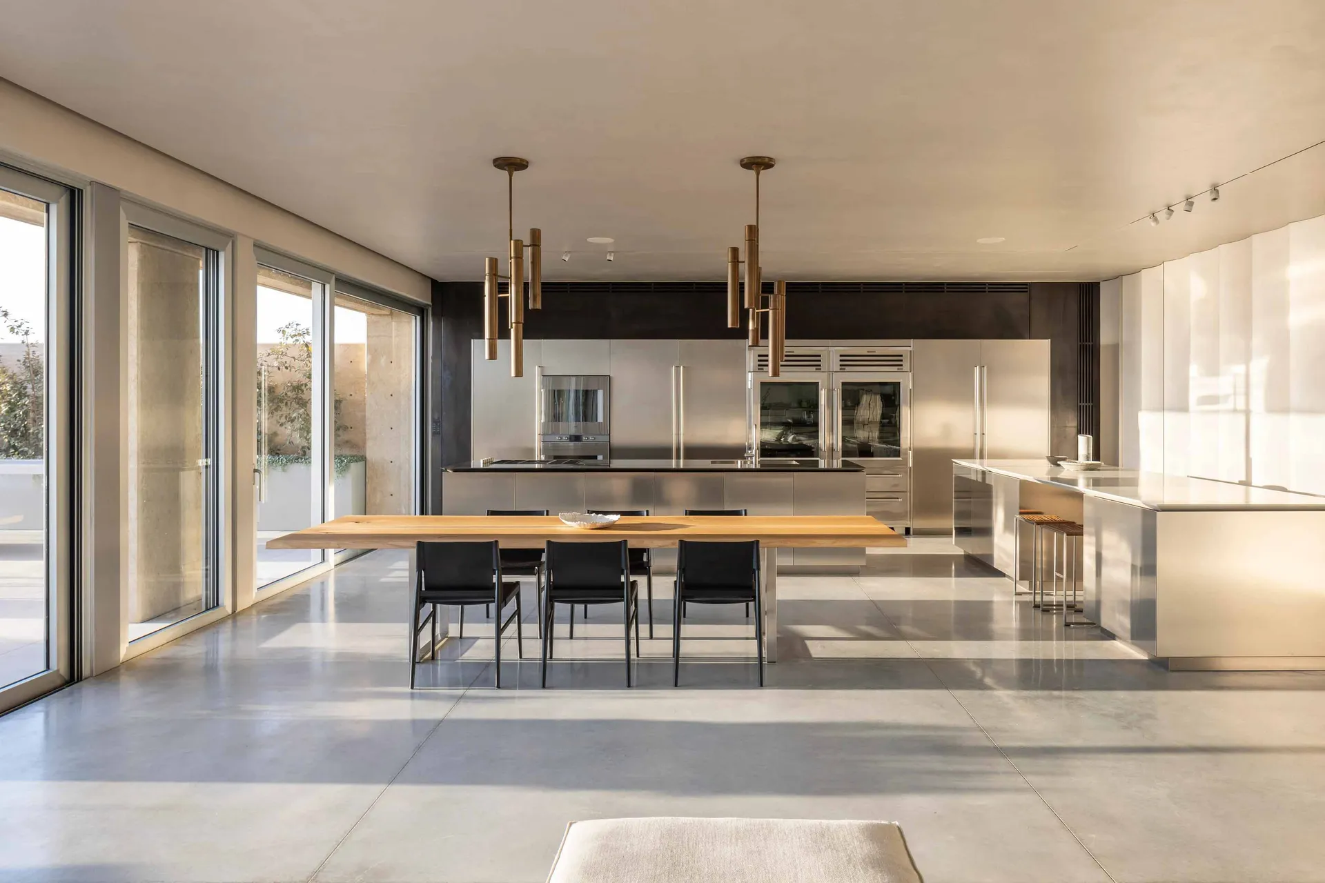 A modern residential kitchen featuring stainless steel cabinets and countertops, with a wooden dining table and black chairs.