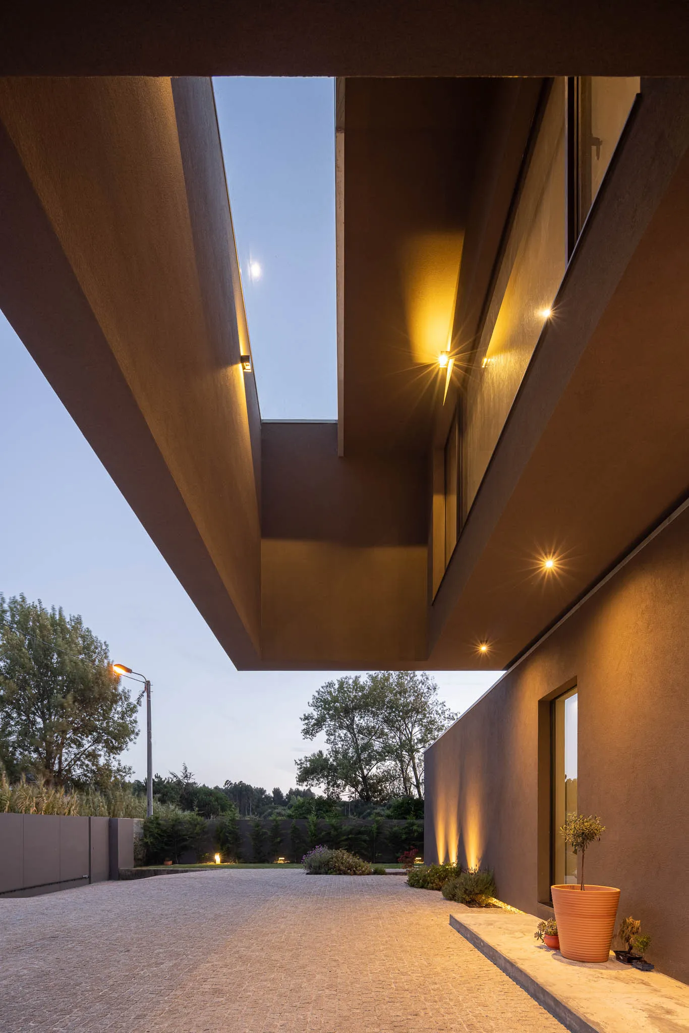 Concrete entrance and pathway leading up to a modern building with a skylight and warm lighting.