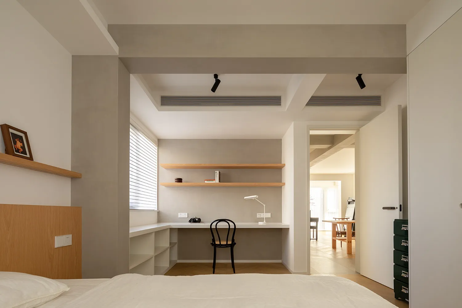 A minimalist bedroom with wooden shelves, a black chair, and a white desk.