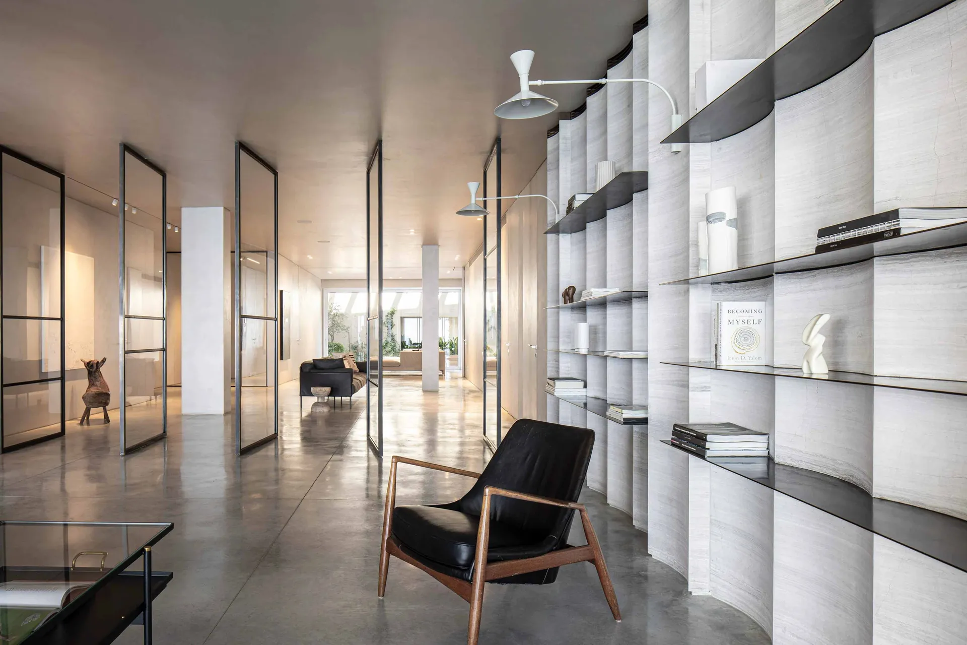 Modern living room featuring minimalist furniture, a sleek black armchair, and a library corner with concrete shelving and gl