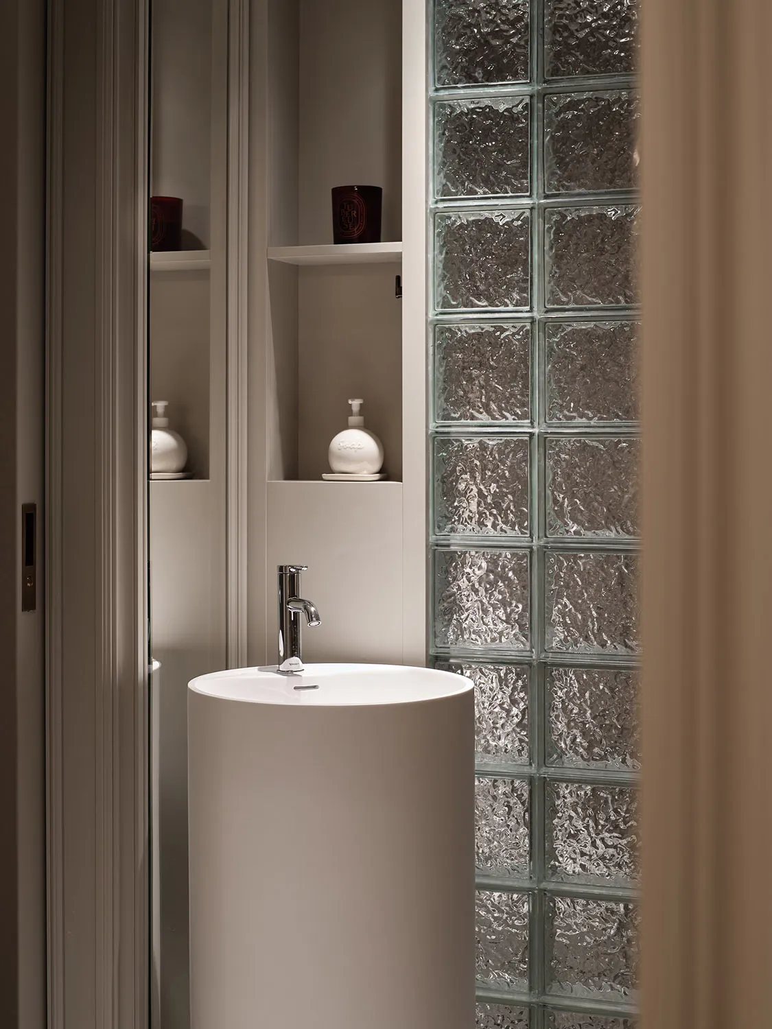 A minimalist bathroom with a glass-brick wall and a round pedestal sink.