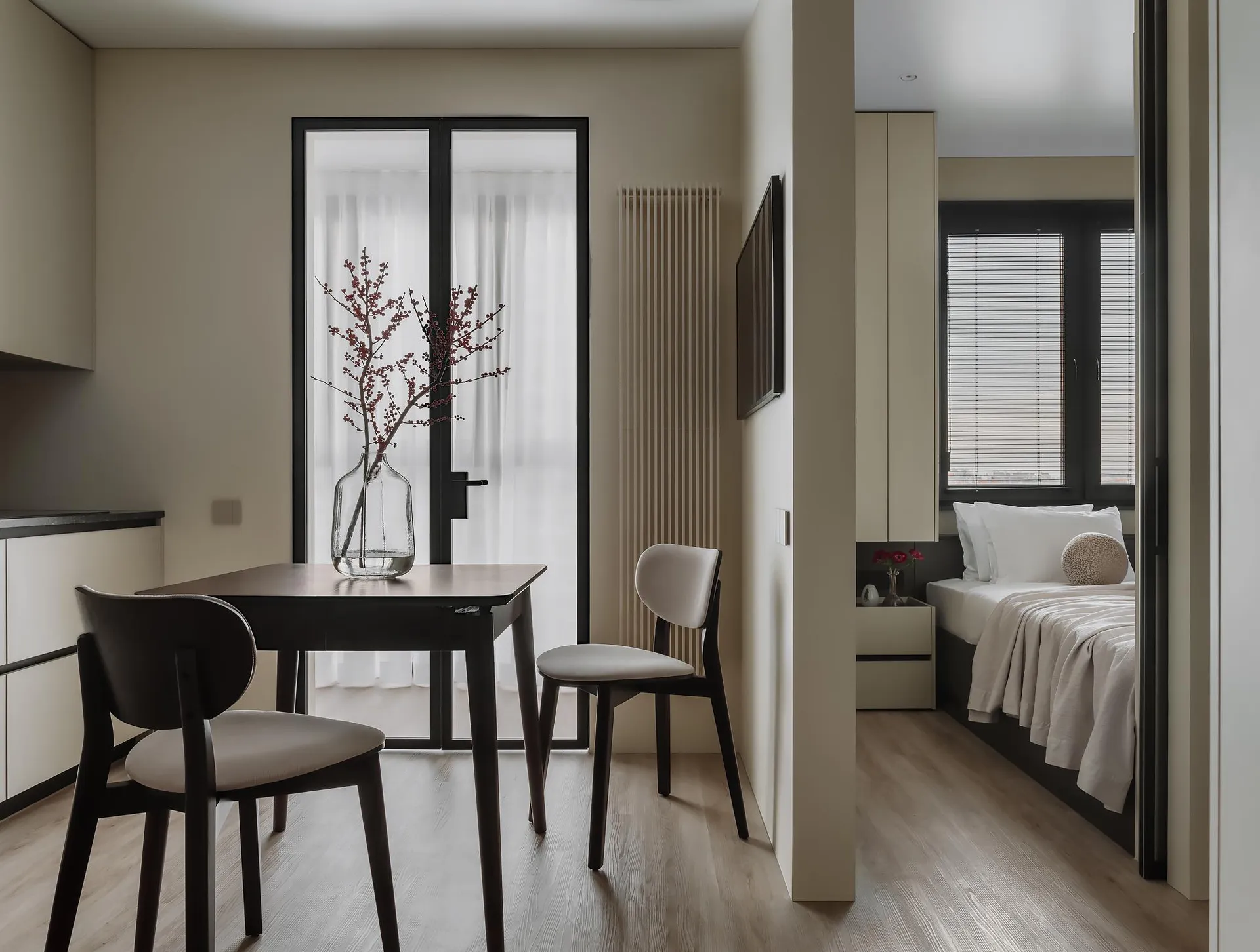 Modern minimalist living space with a wooden table, chairs, and vase with flowers.