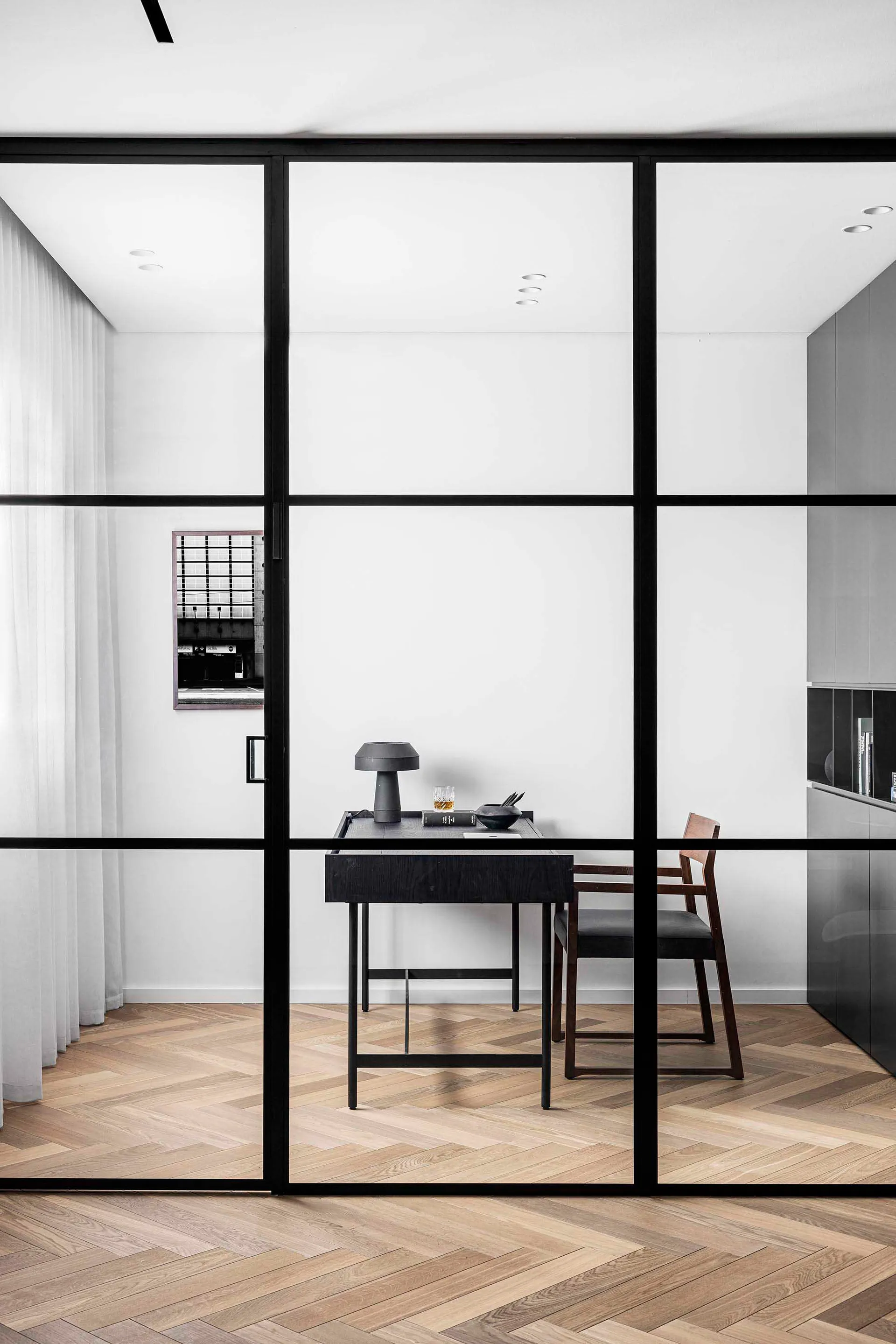 A sleek office space featuring a minimalist design with glass walls and wooden flooring.
