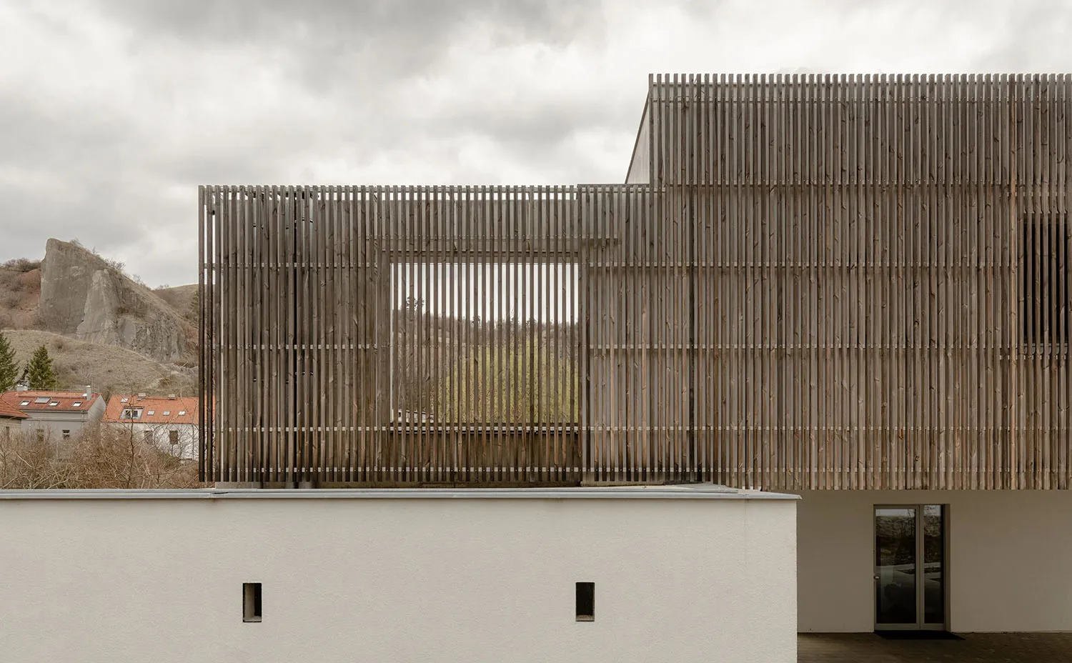 A modern wooden building with a slatted facade overlooking a natural landscape.
