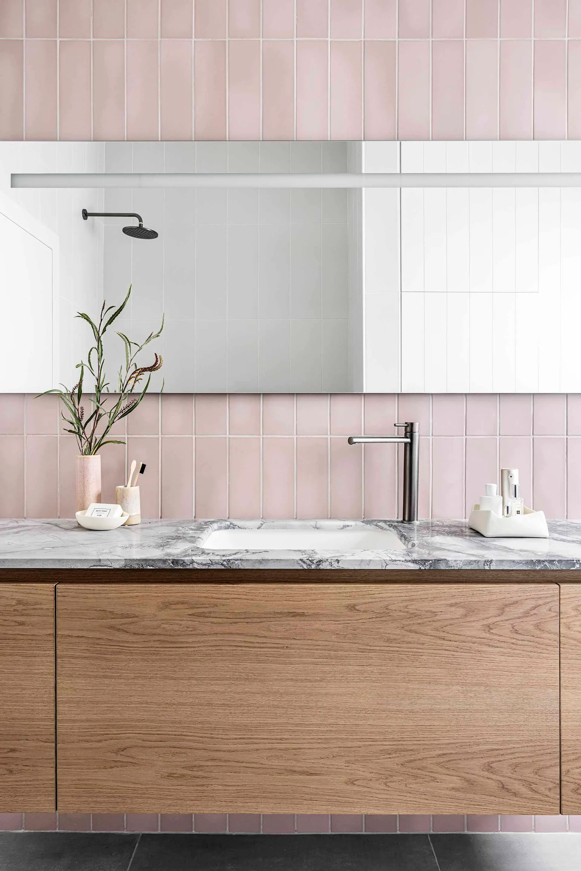 A minimalist bathroom with ceramic tiles features a vanity with a marble countertop, a wooden cabinet, a white sink, a mirror
