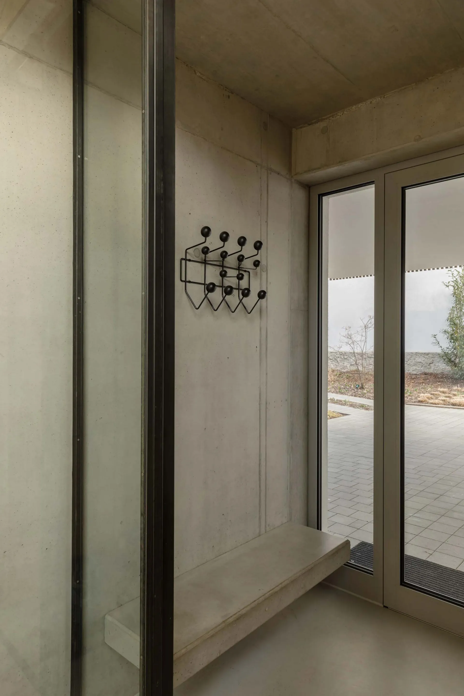 Modern minimalist entryway featuring concrete materials with a unique black coat hanger