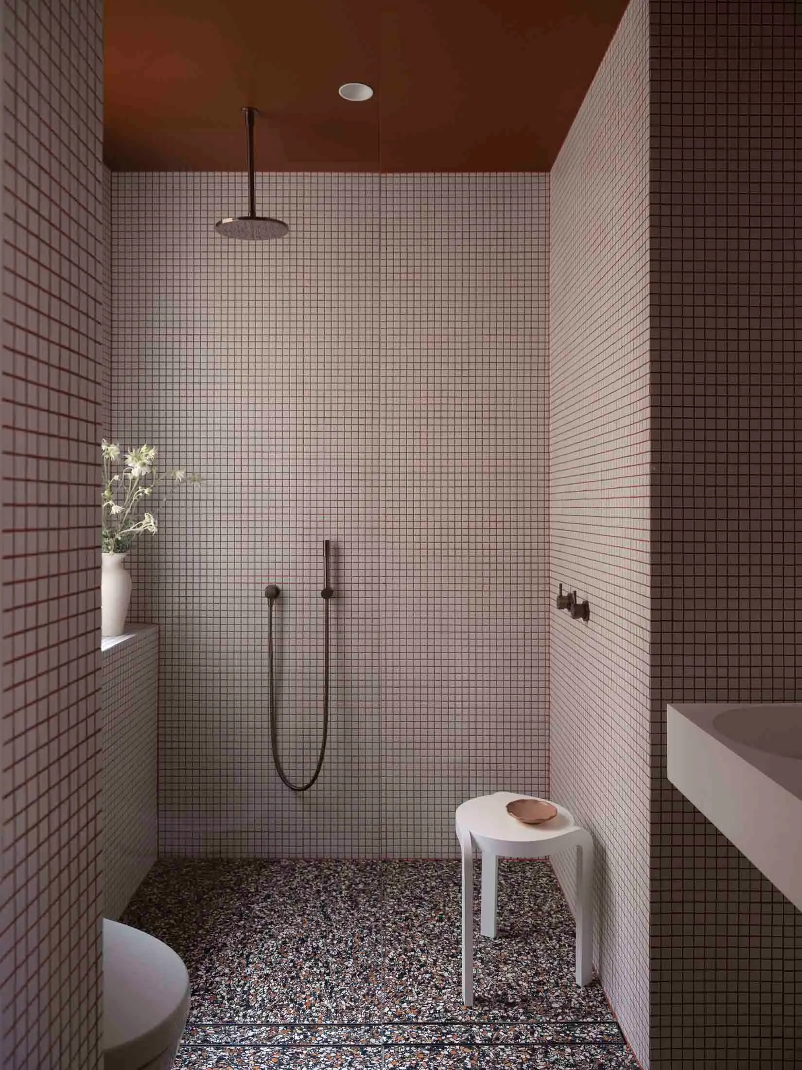 A modern bathroom with white and black terrazzo tiles on the floor, white walls covered in small square tiles, and a white to