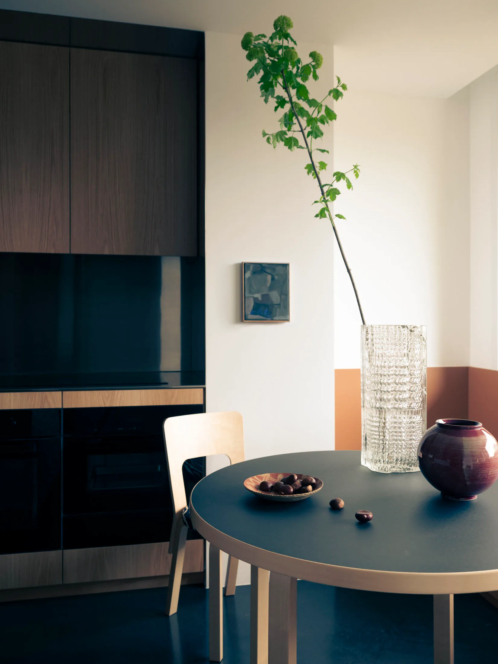 Modern black kitchen with wooden furniture, featuring a round dining table and a vase with greenery.