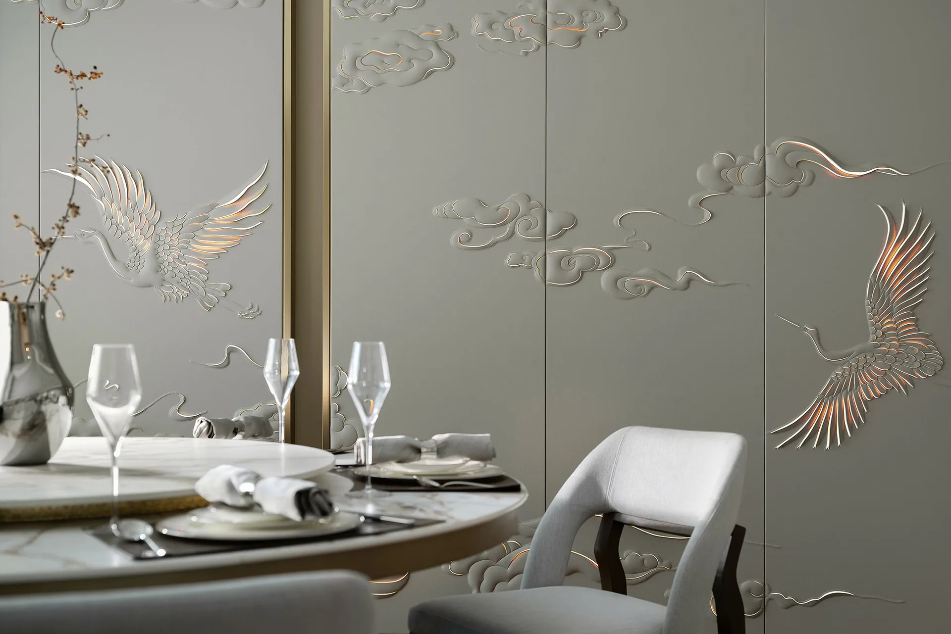 A modern dining room featuring metallic texture wall panels with bird and cloud motifs, table setting, and wine glasses.