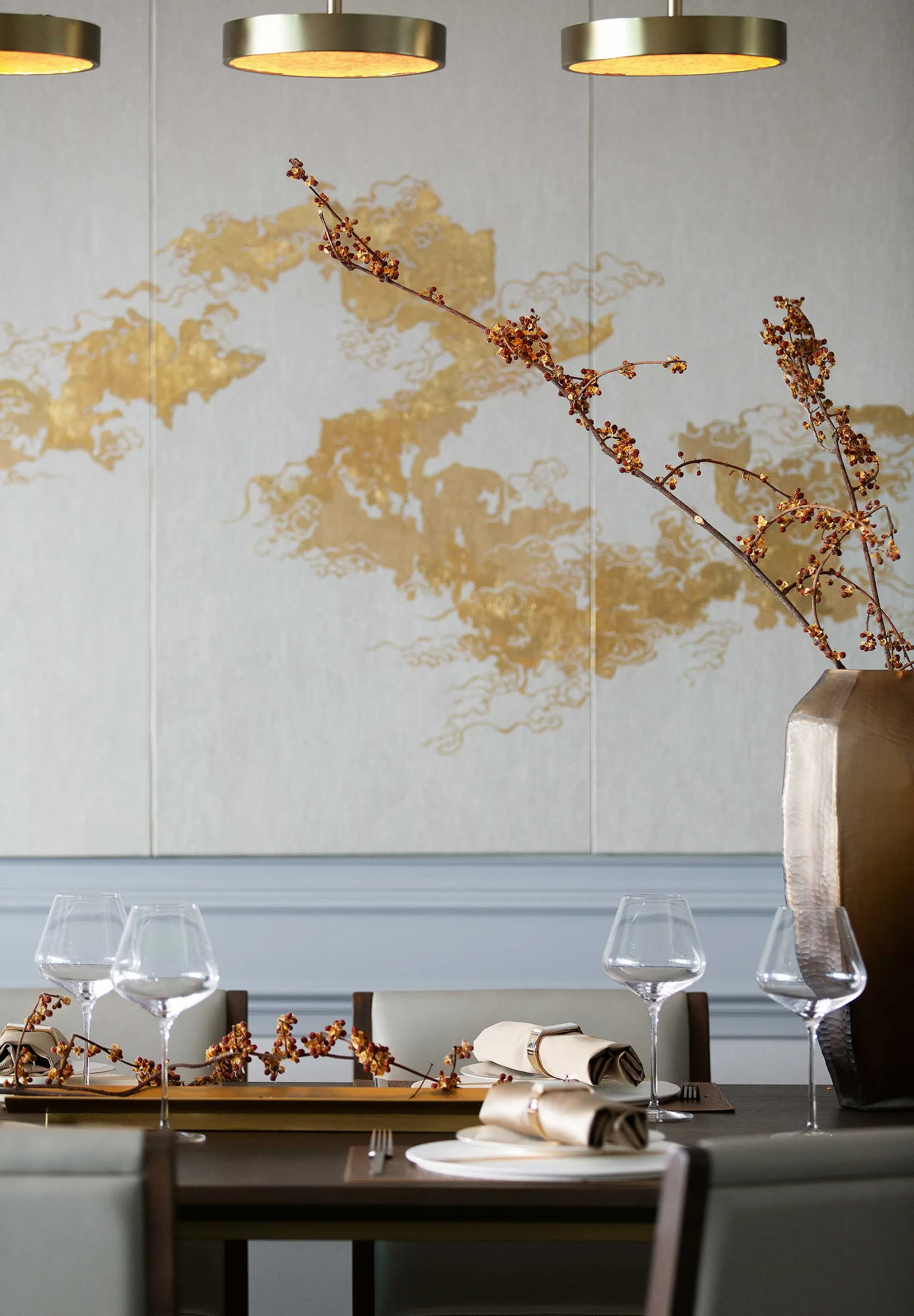 Modern restaurant dining area featuring metallic pendant lights and decorative branches in a vase.